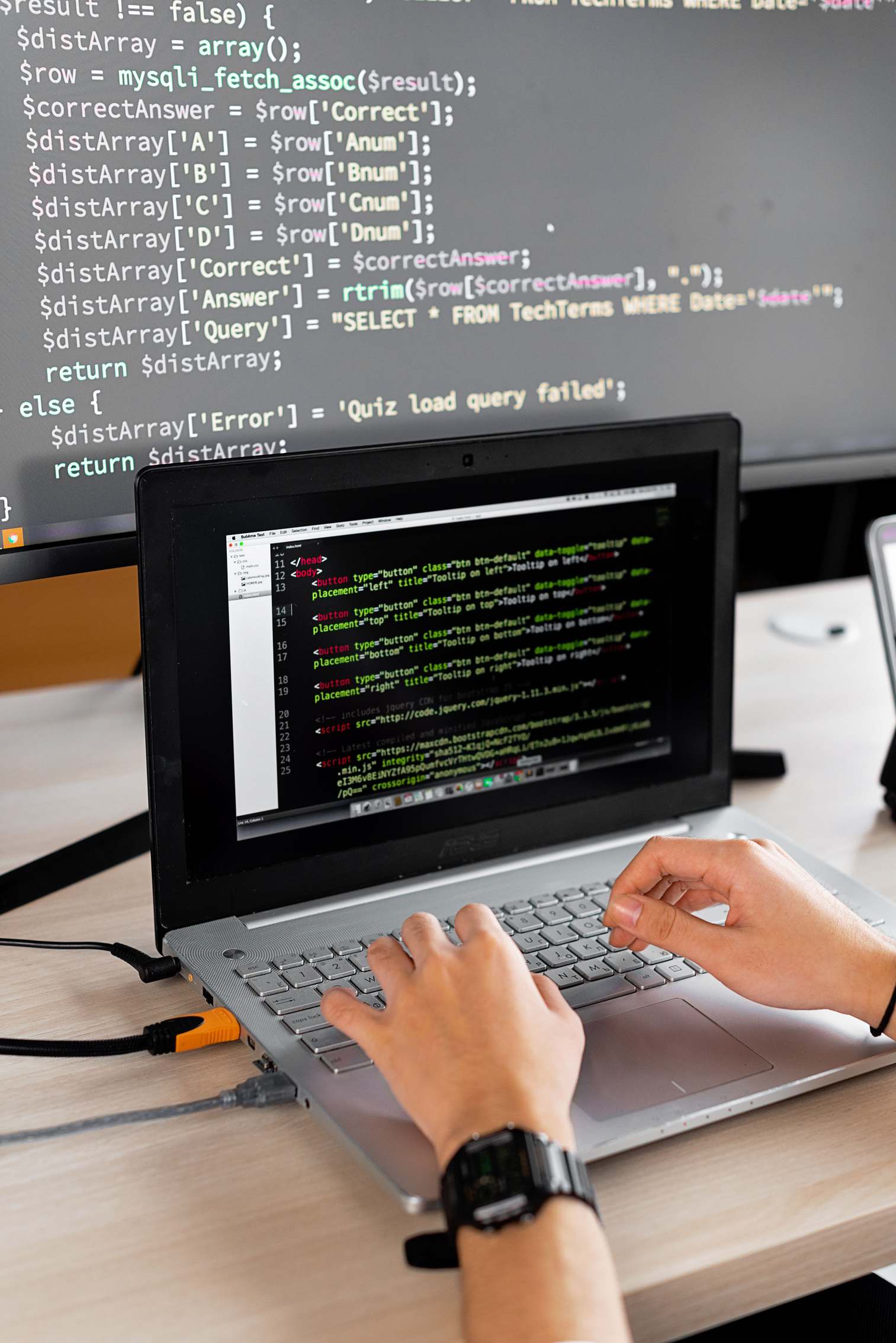 Person, die an einem Schreibtisch mit Laptop und externem Monitor Programmcode schreibt