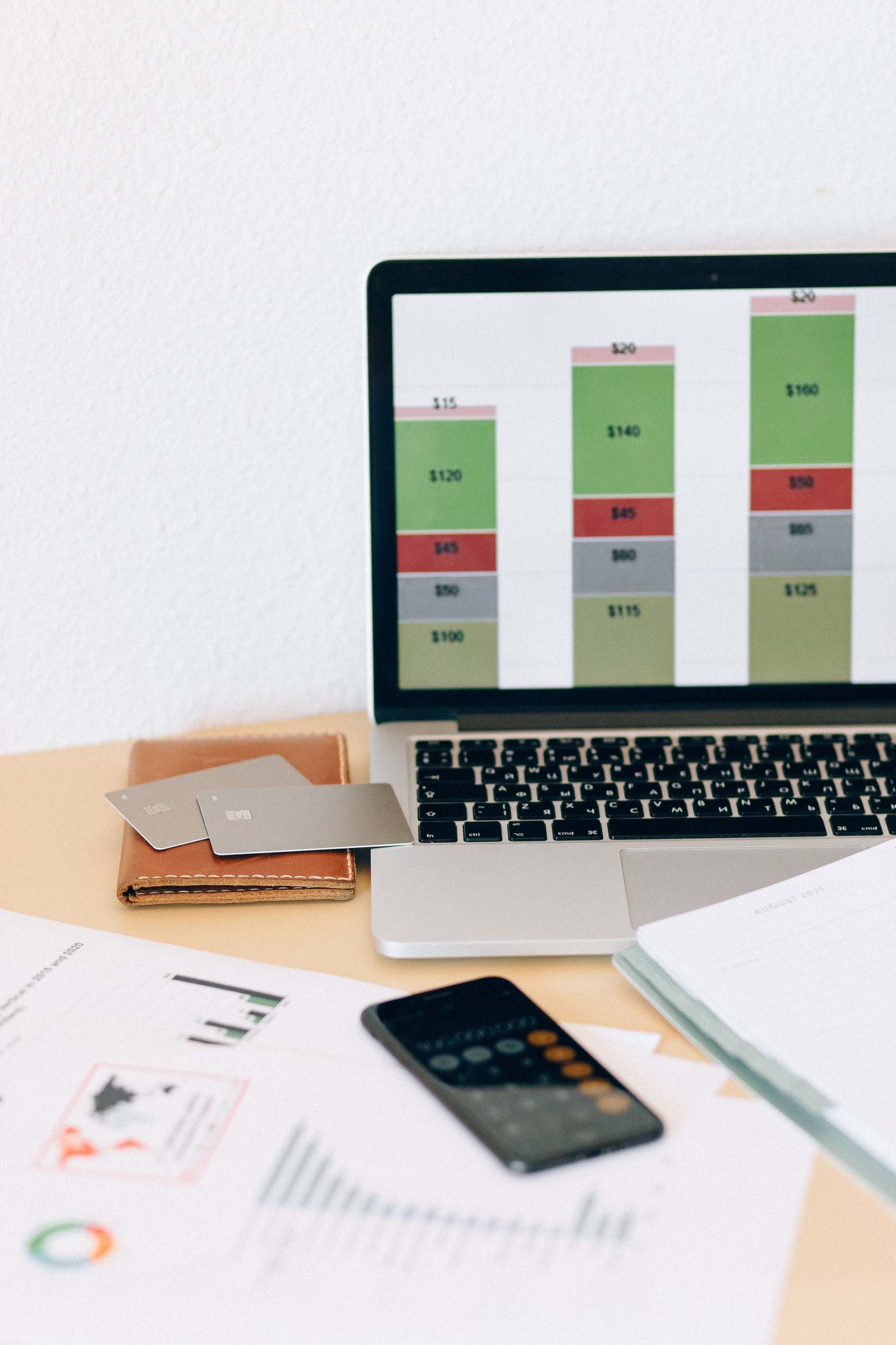 Laptop mit Finanzchart neben Unterlagen und Karten auf einem Schreibtisch